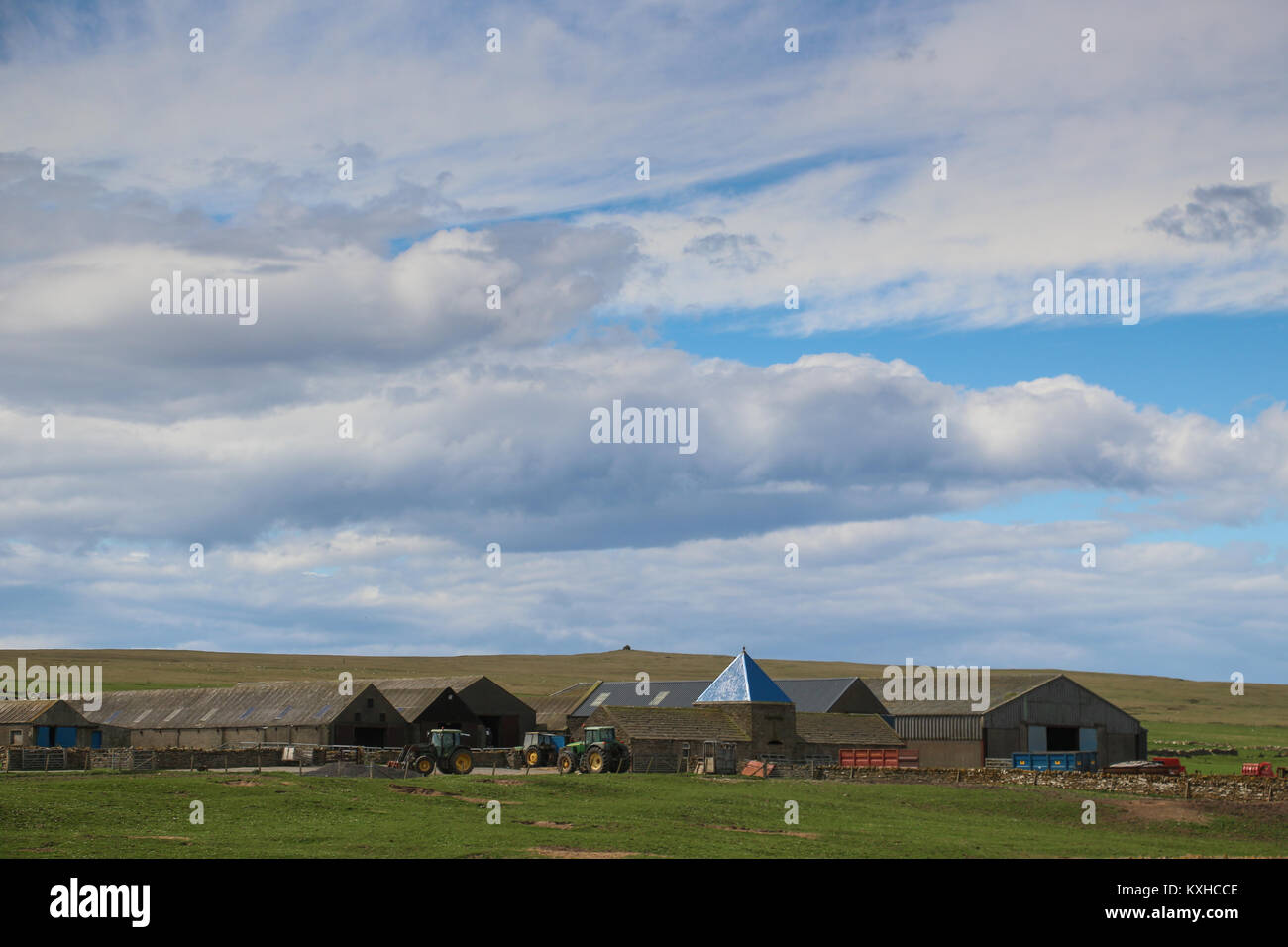 Large, working farm near Skaill House on Orkney Island, Scotland, United Kingdom with many barns, farm equipment, under a huge blue cloud-filled sky. Stock Photo