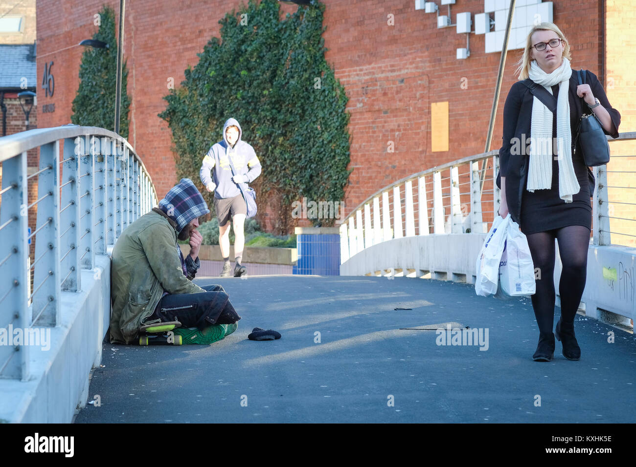 A homeless man begs on Centenary Bridge, Leeds, UK in winter, as commuters pass by. UK housing crisis 2018. The social divide. Stock Photo