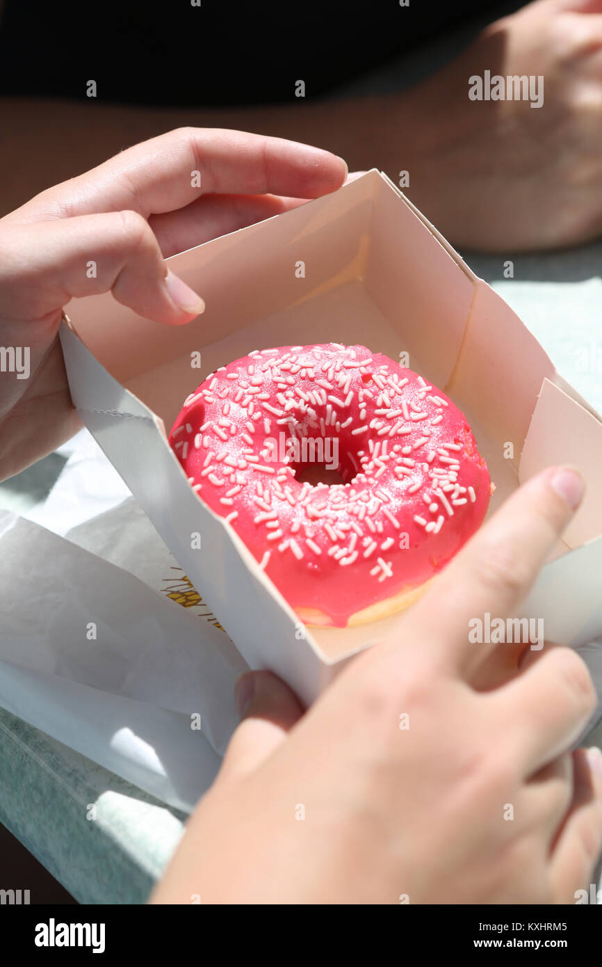 Round pink iced donut in a box on a persons lap Stock Photo