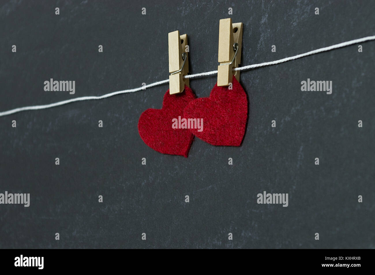 Red hearts hanging at an angle from clothespin in front of chalkboard background Stock Photo