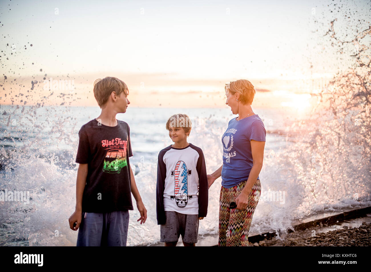 two brothers with her mother at the sea side looking at waves splashing Stock Photo