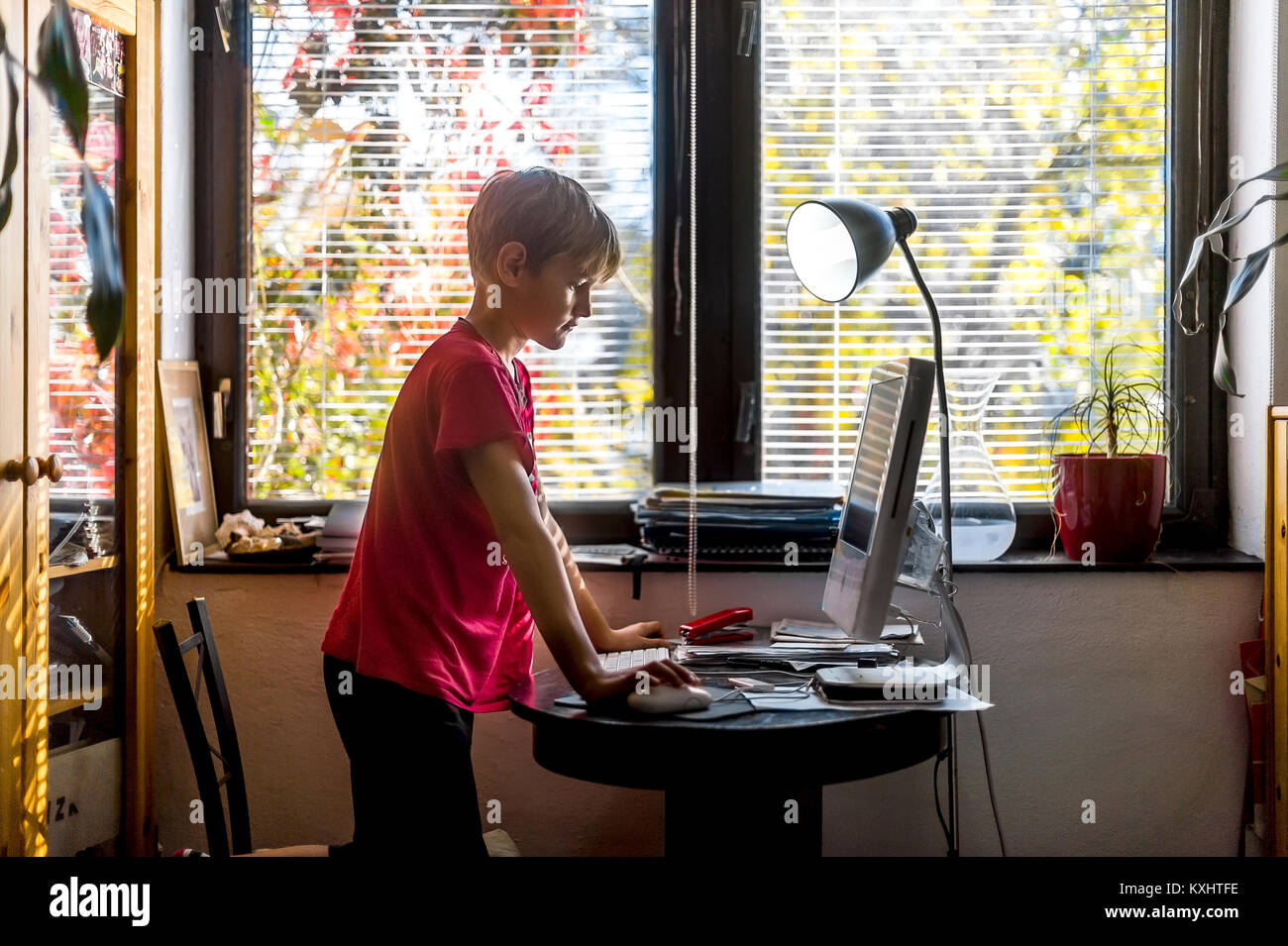 young boy in red T-shirt sitting in front of PC at home Stock Photo