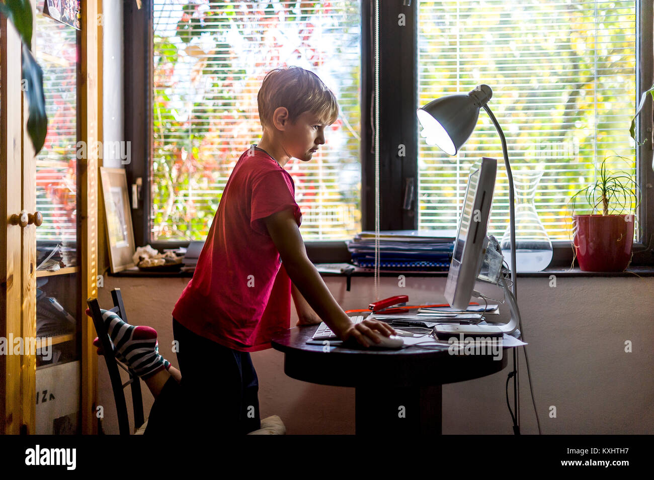 young boy in red T-shirt sitting in front of PC at home Stock Photo