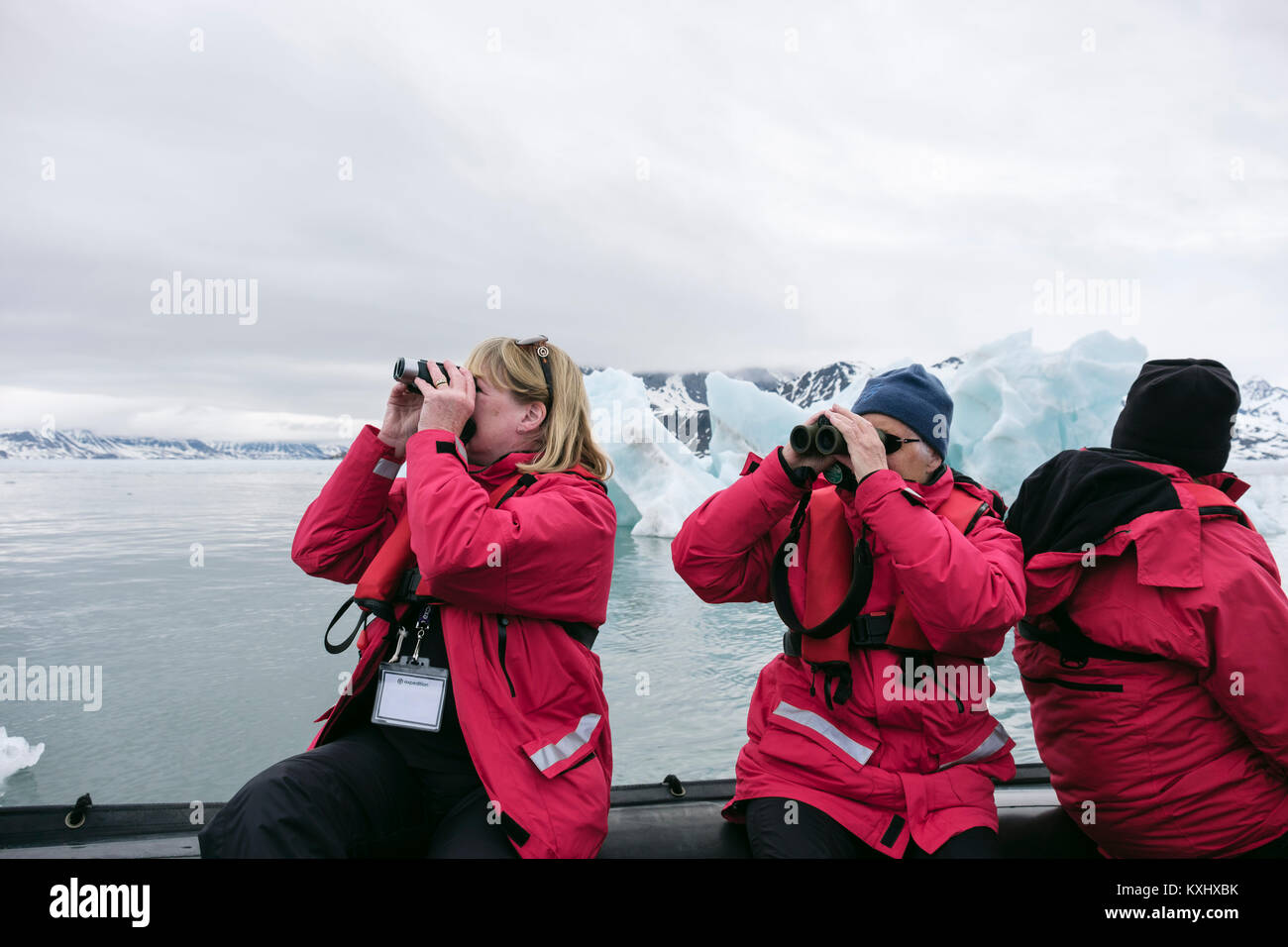 G Adventures cruise ship passengers watching wildlife using binoculars on a Zodiac dinghy in icy Arctic waters. Spitsbergen, Svalbard, Norway Stock Photo