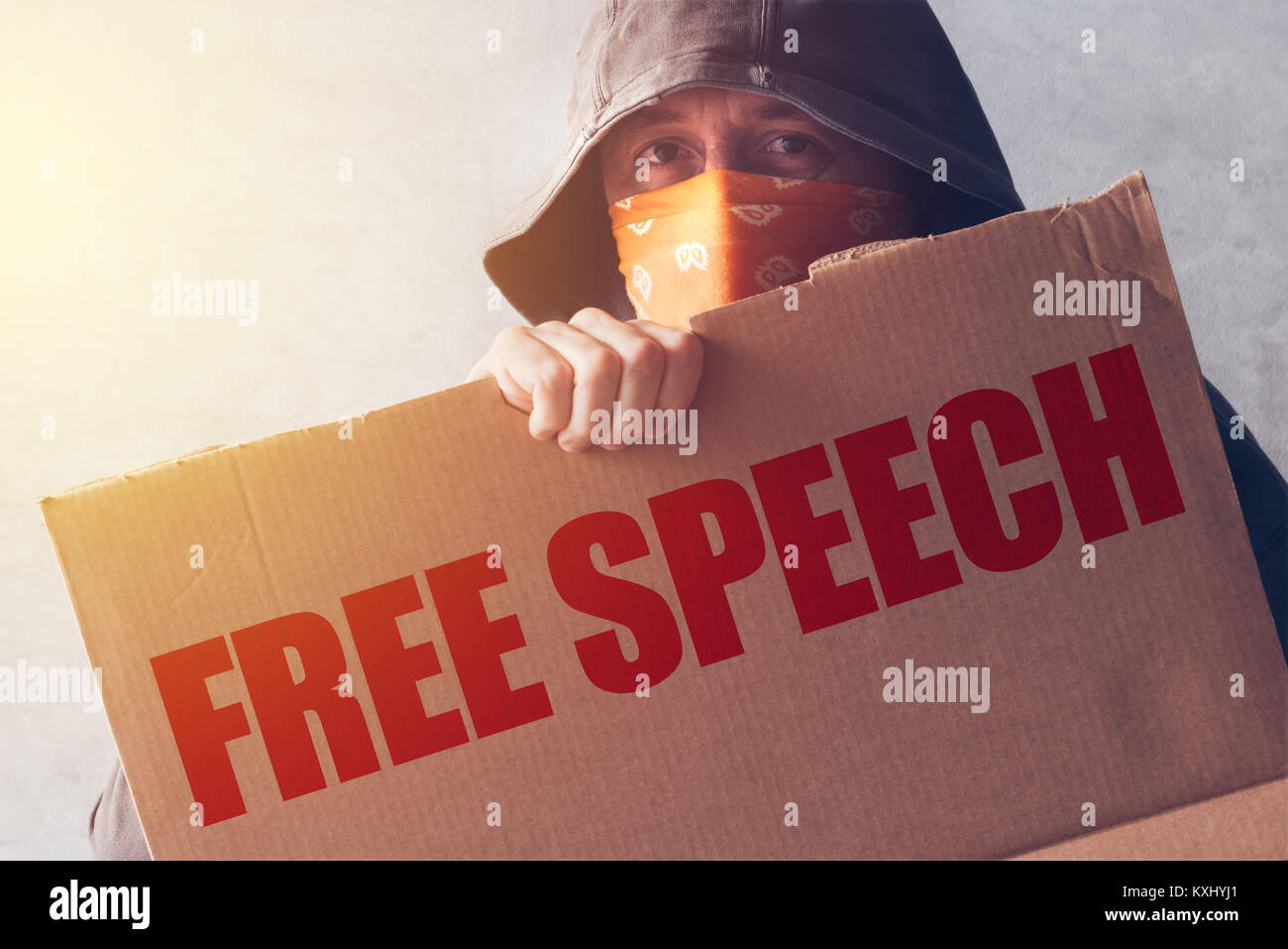 Hooded activist protestor holding Free Speech protest sign. Man with hoodie and scarf over face taking part in activism and fighting for the cause. Stock Photo