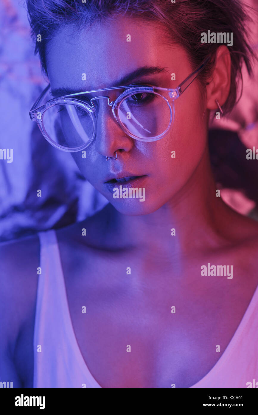 Beautiful young woman wearing eyeglasses in illuminated studio Stock Photo