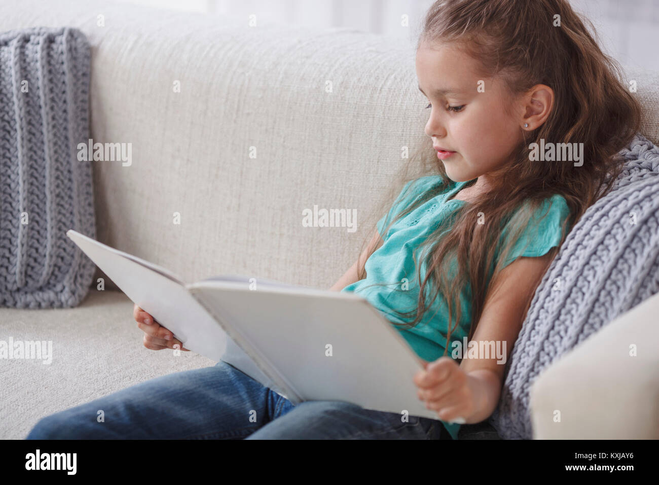 Girl reading book while sitting on sofa at home Stock Photo