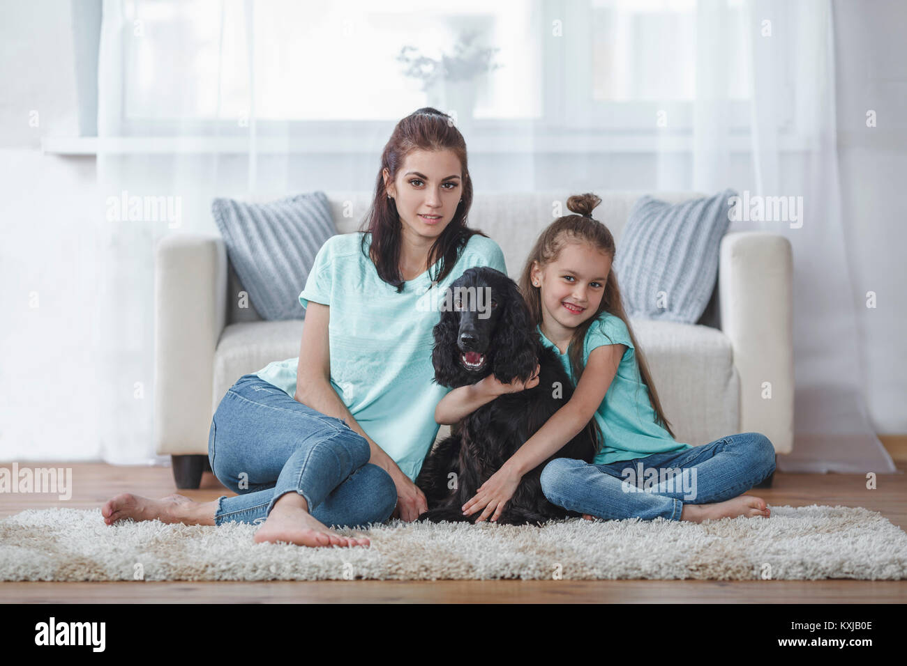Portrait of mother and daughter with dog sitting on rug at home Stock Photo