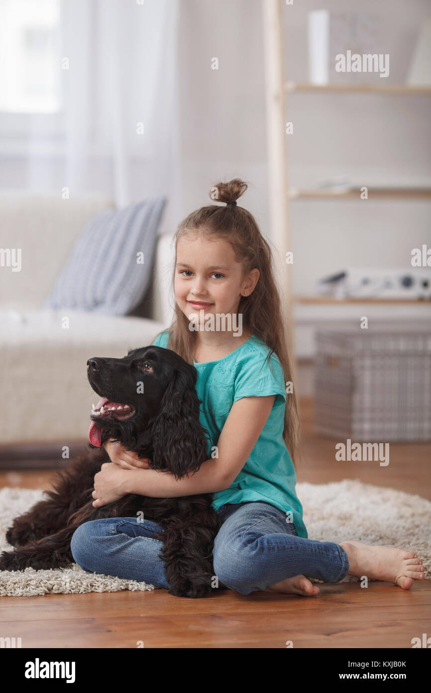 Portrait of cute girl embracing dog while sitting on rug at home Stock Photo