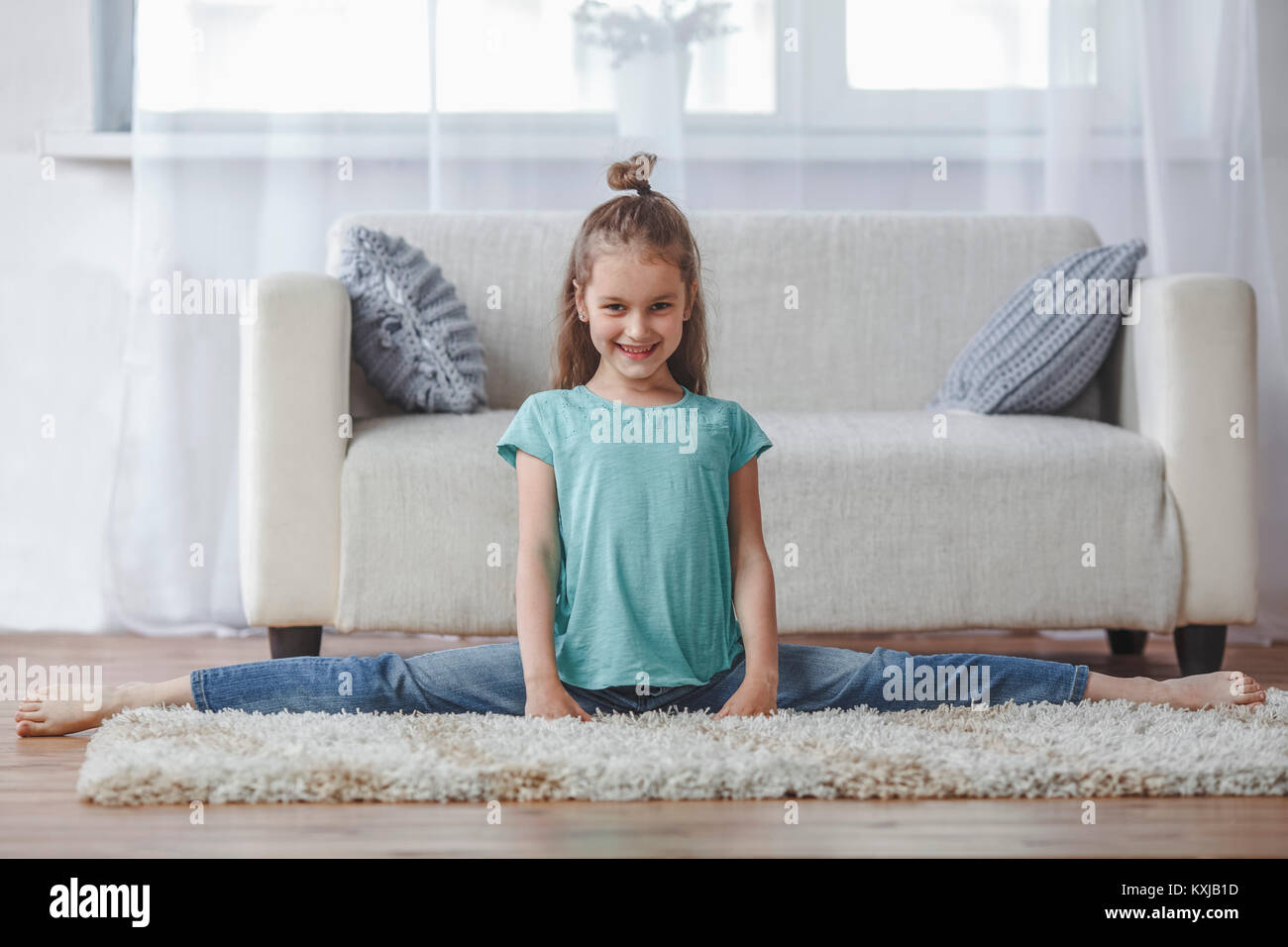 Full length portrait of smiling girl doing splits on rug in living room at home Stock Photo