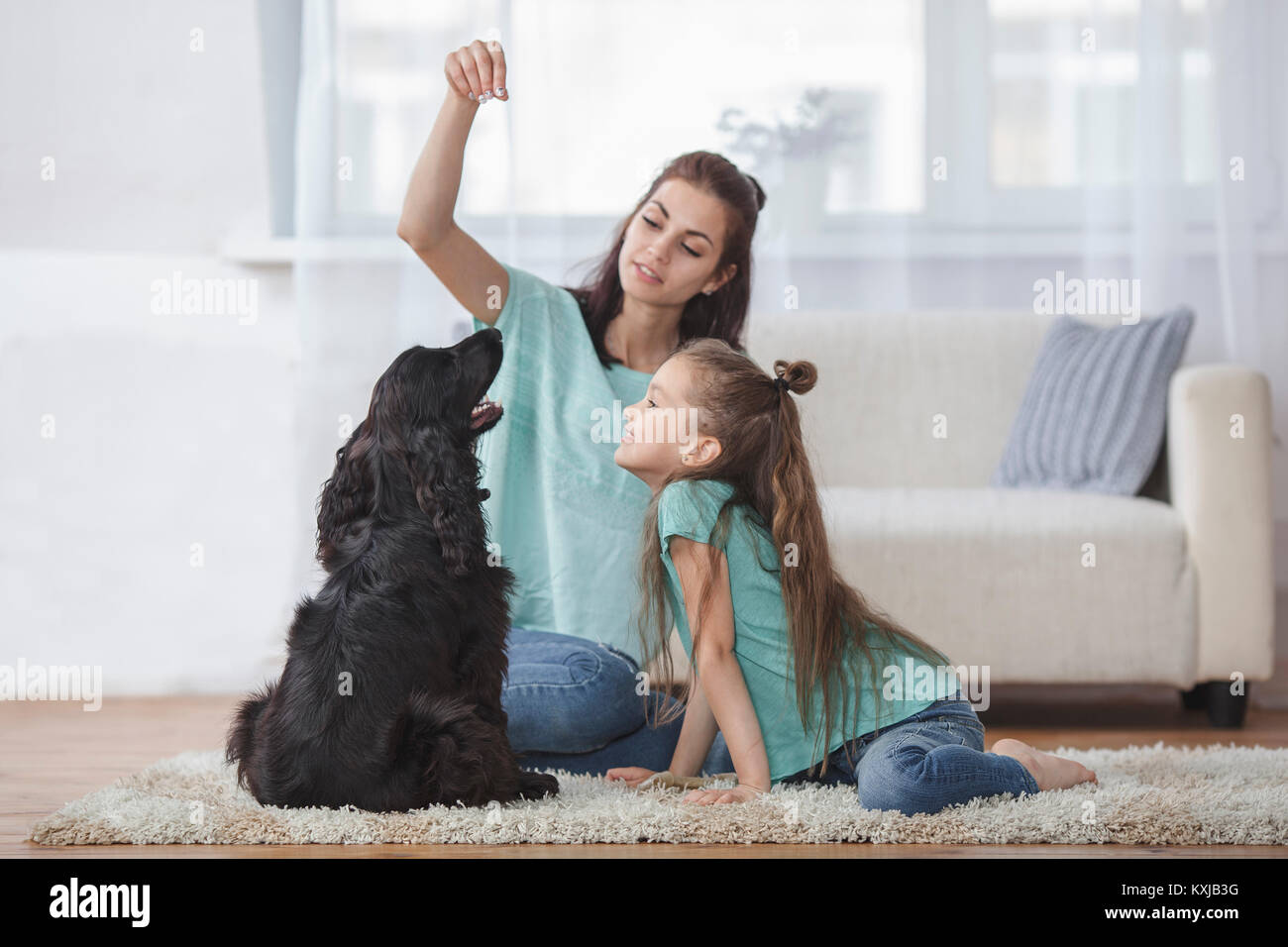 Mother and daughter playing with dog in living room at home Stock Photo