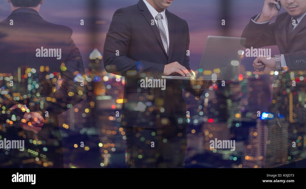double exposure of Businessman group standing and working in night office over the cityscape phoro blurred background, business hard working concept Stock Photo