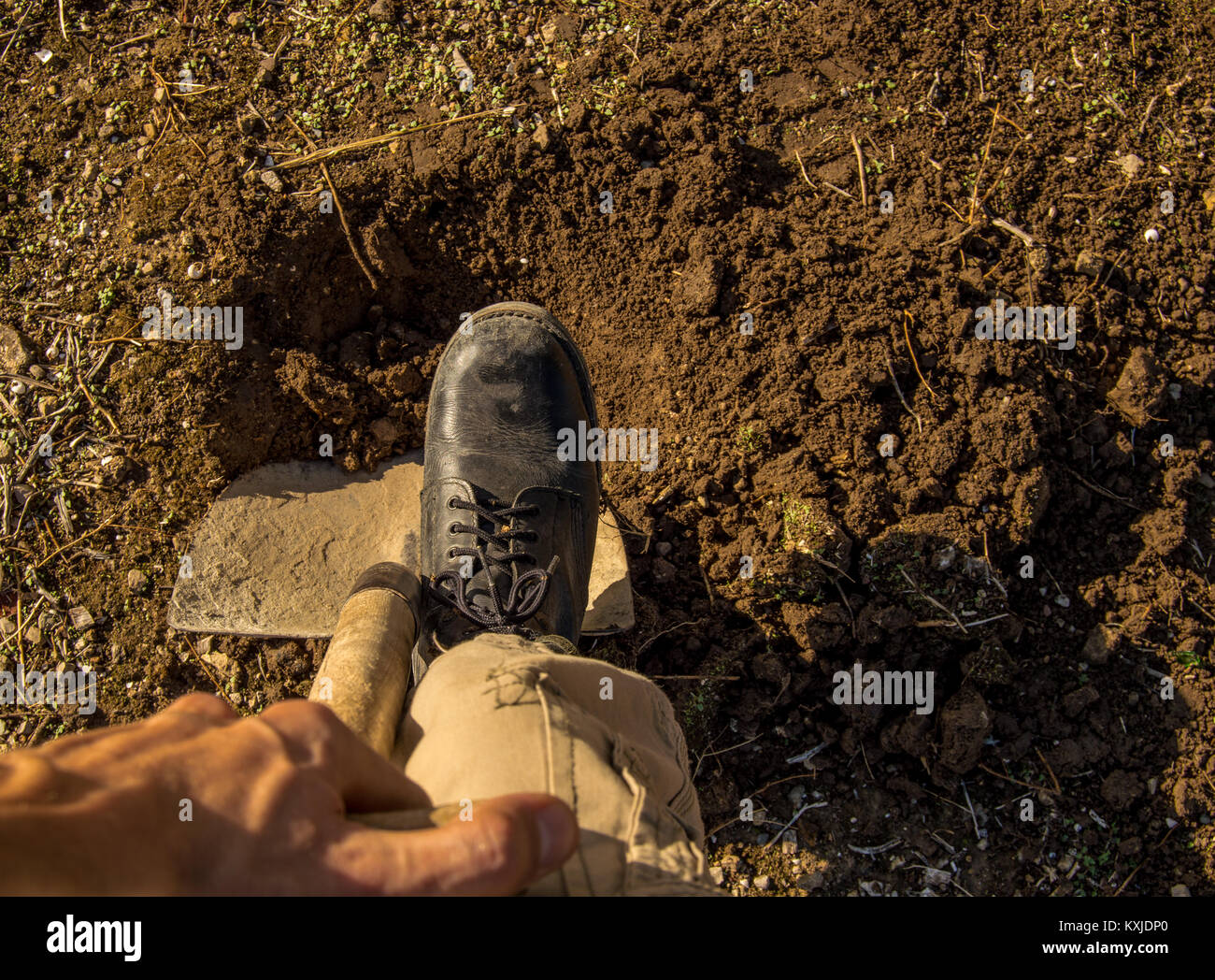 Digging a hole with shovel and black boots in a rural village. Man's