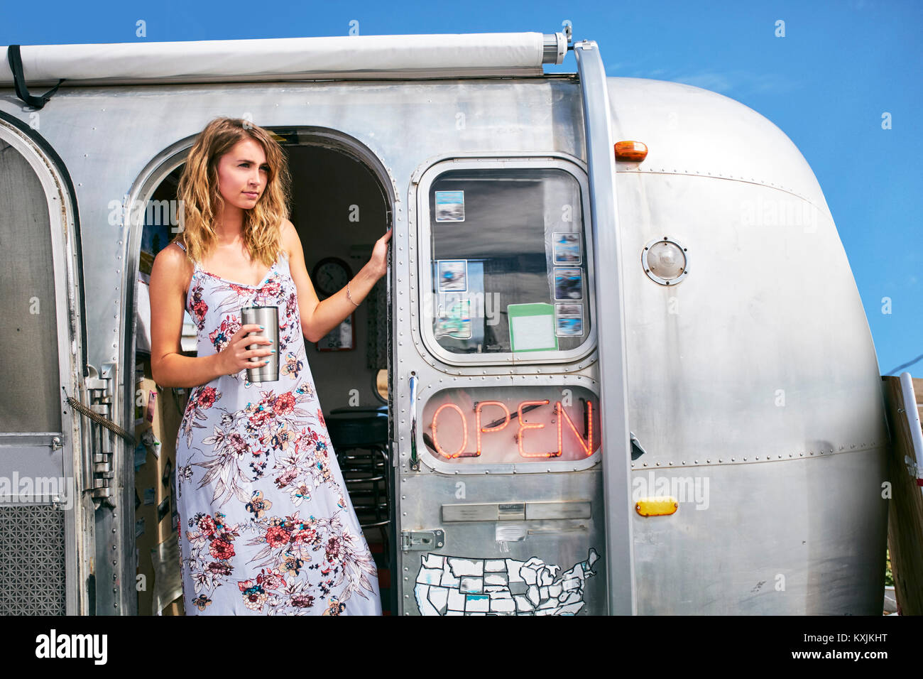 Young woman with coffee looking out from airstream  coffee shop doorway Stock Photo