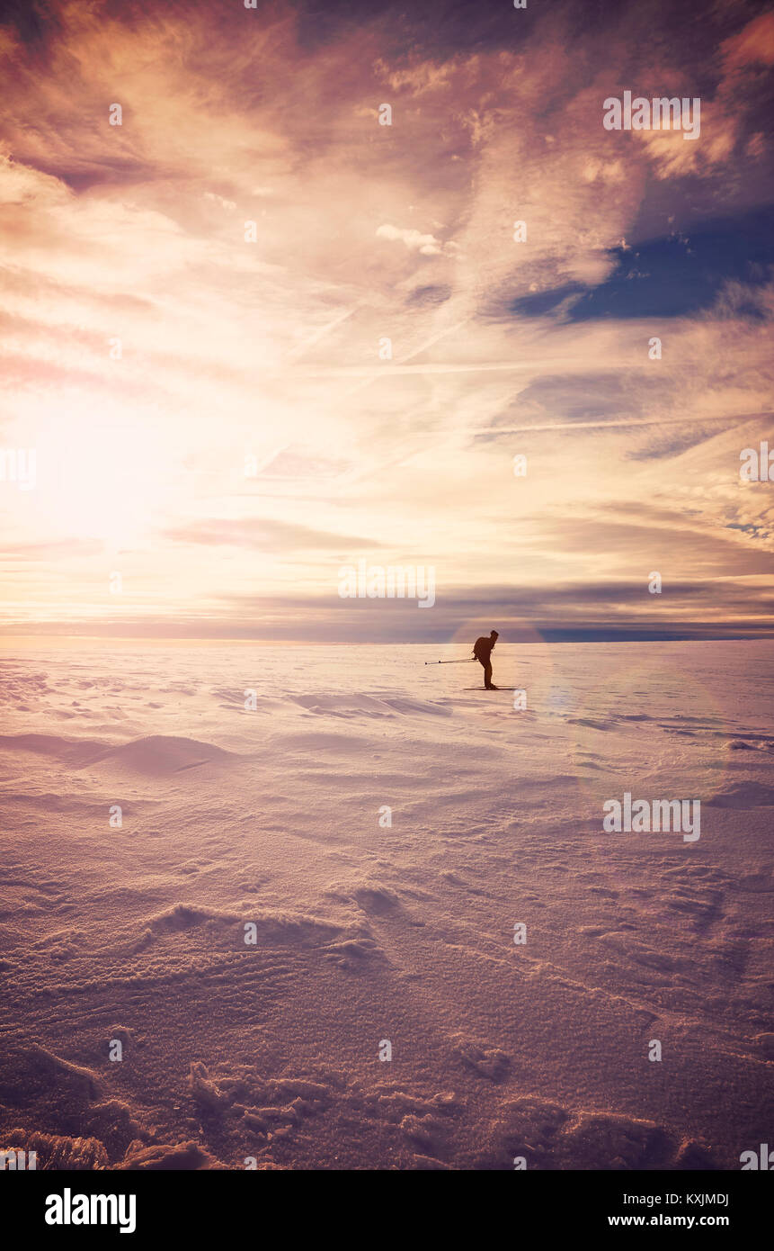 Winter mountain landscape with cross-country skier silhouette at sunset, lens flare effect, color toned picture, Karkonosze National Park, Poland. Stock Photo