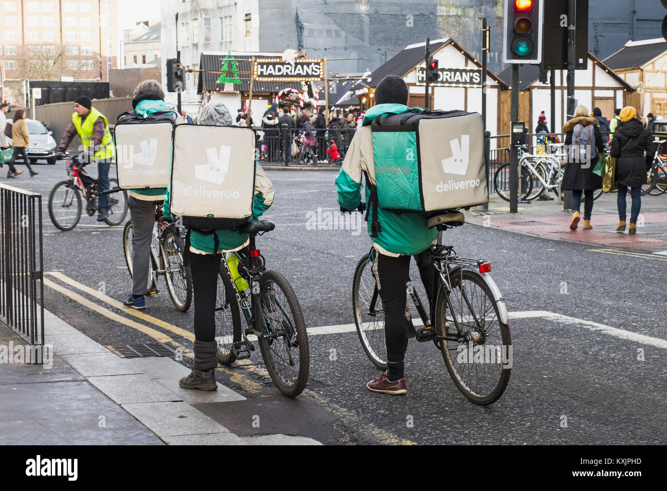 Three Deliveroo cyclists wait for traffic lights to change to green on a Newcastle upon Tyne street whilst delivering or collecting food orders. Stock Photo