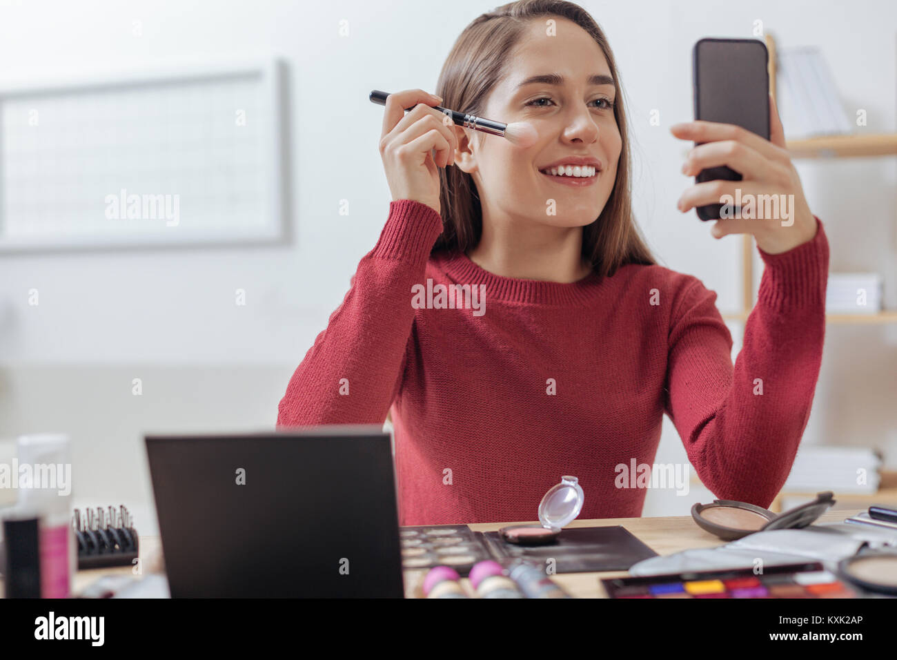 Beautiful young woman putting on facial powder and smiling Stock Photo ...