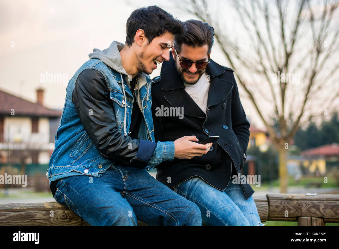 Two young men sitting reading sms text message Stock Photo