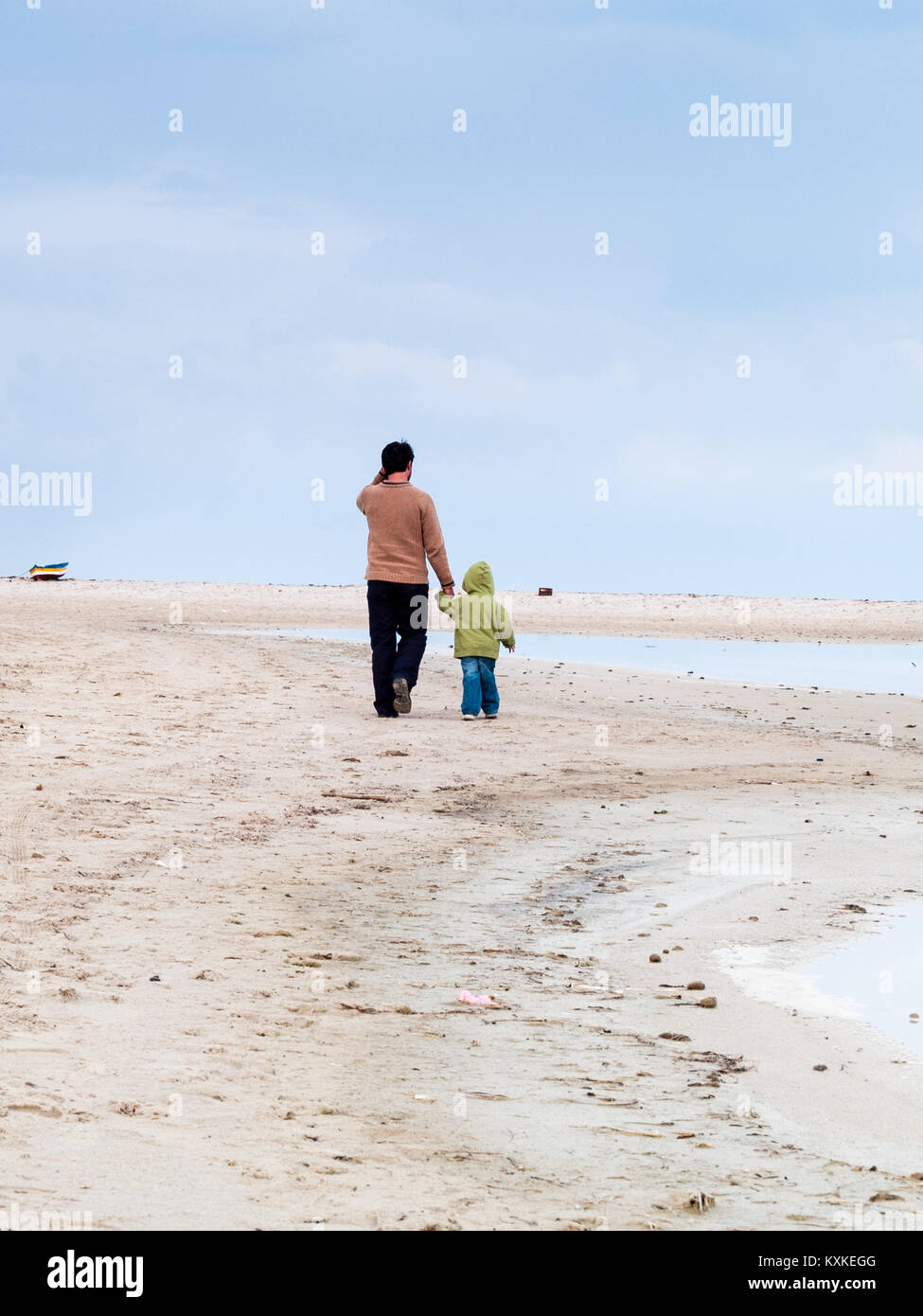 Djerba, Tunisia father and son walk on the beach holding hands cloudy and dark sky in winter Stock Photo