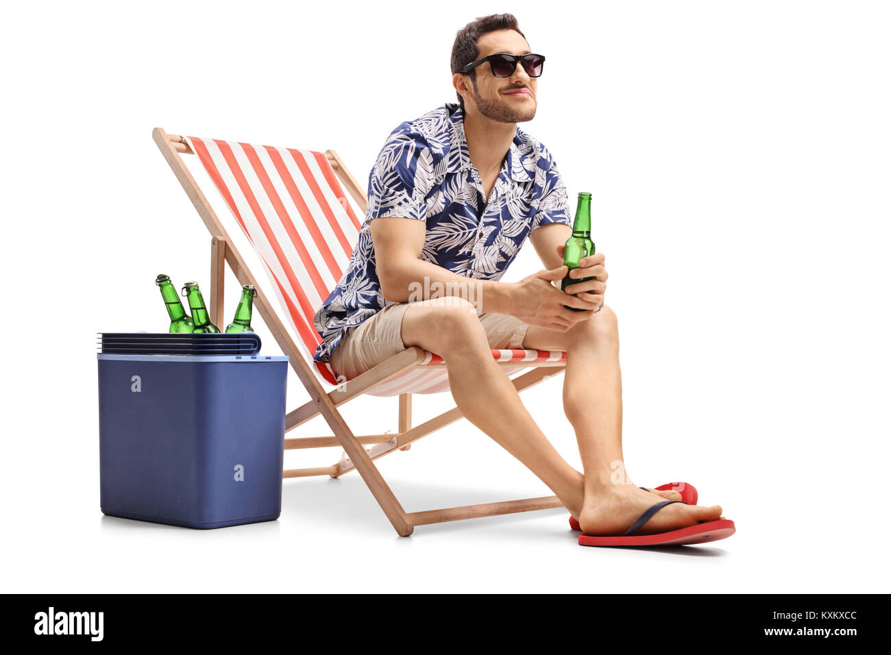 Tourist with a beer bottle sitting in a deck chair next to a cooling box and looking away isolated on white background Stock Photo