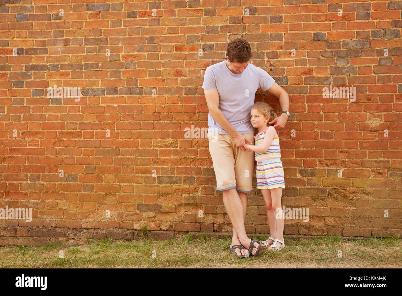 Girl and father leaning against brick wall Stock Photo