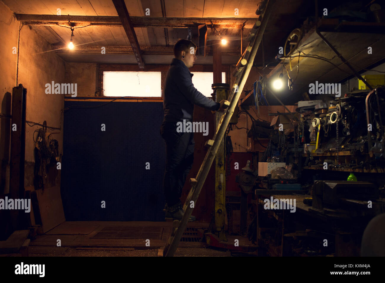 Mechanic on ladder looking at shelves in workshop Stock Photo