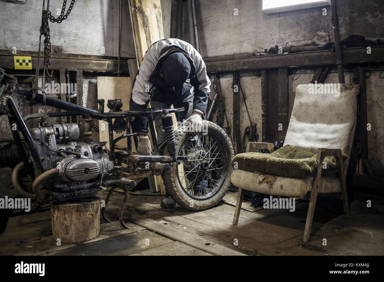Mechanic adjusting wheel on dismantled vintage motorcycle in workshop Stock Photo