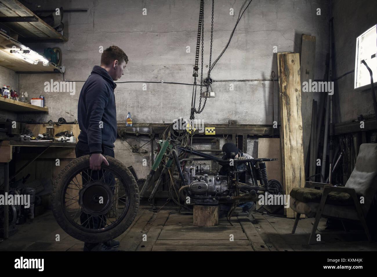 Mechanic carrying vintage motorcycle wheel in workshop Stock Photo