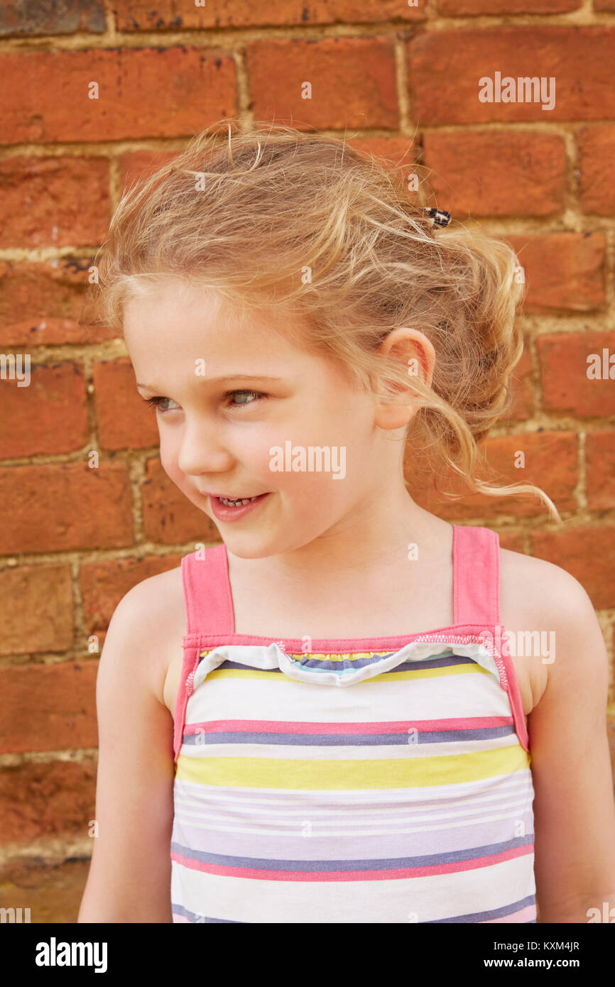 Girl with blond pony tail looking away by brick wall Stock Photo