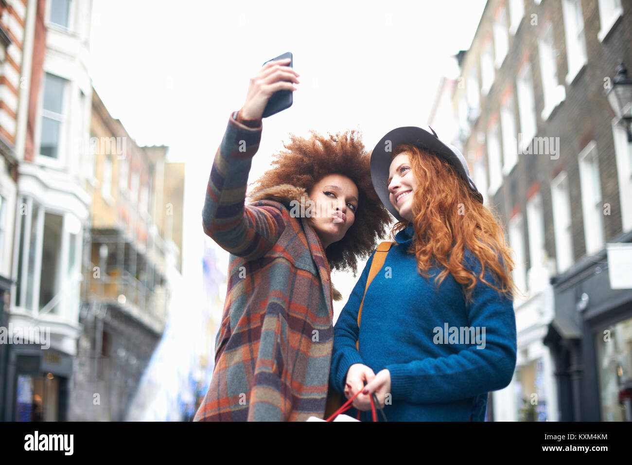 Two young women in street,taking selfie,using smartphone,low angle view Stock Photo