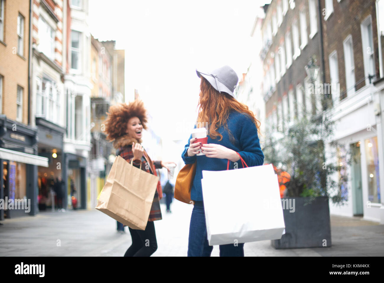 Two young women,holding shopping bags,passing each other in street Stock Photo