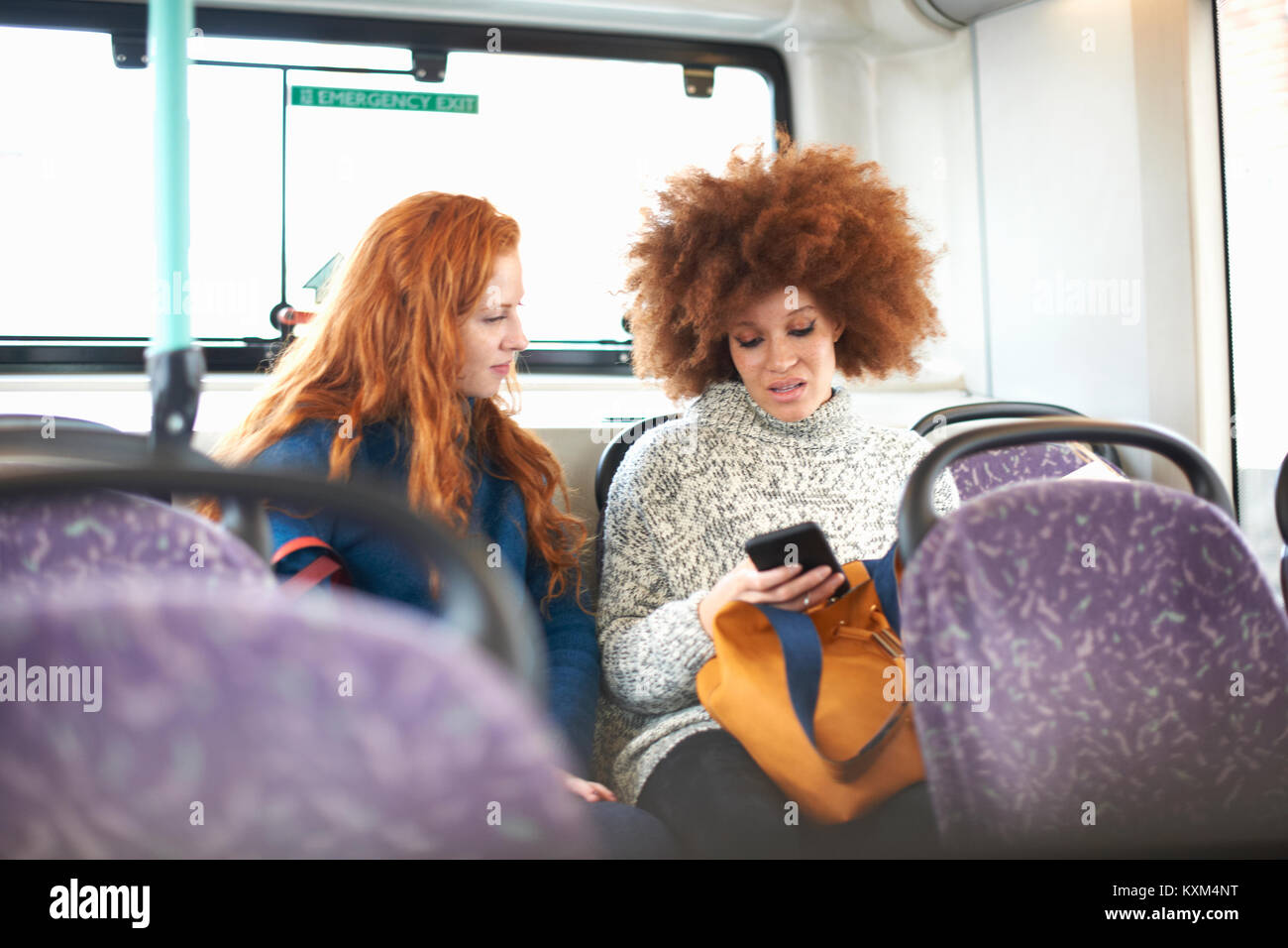 Two young women sitting on bus,looking at smartphone Stock Photo