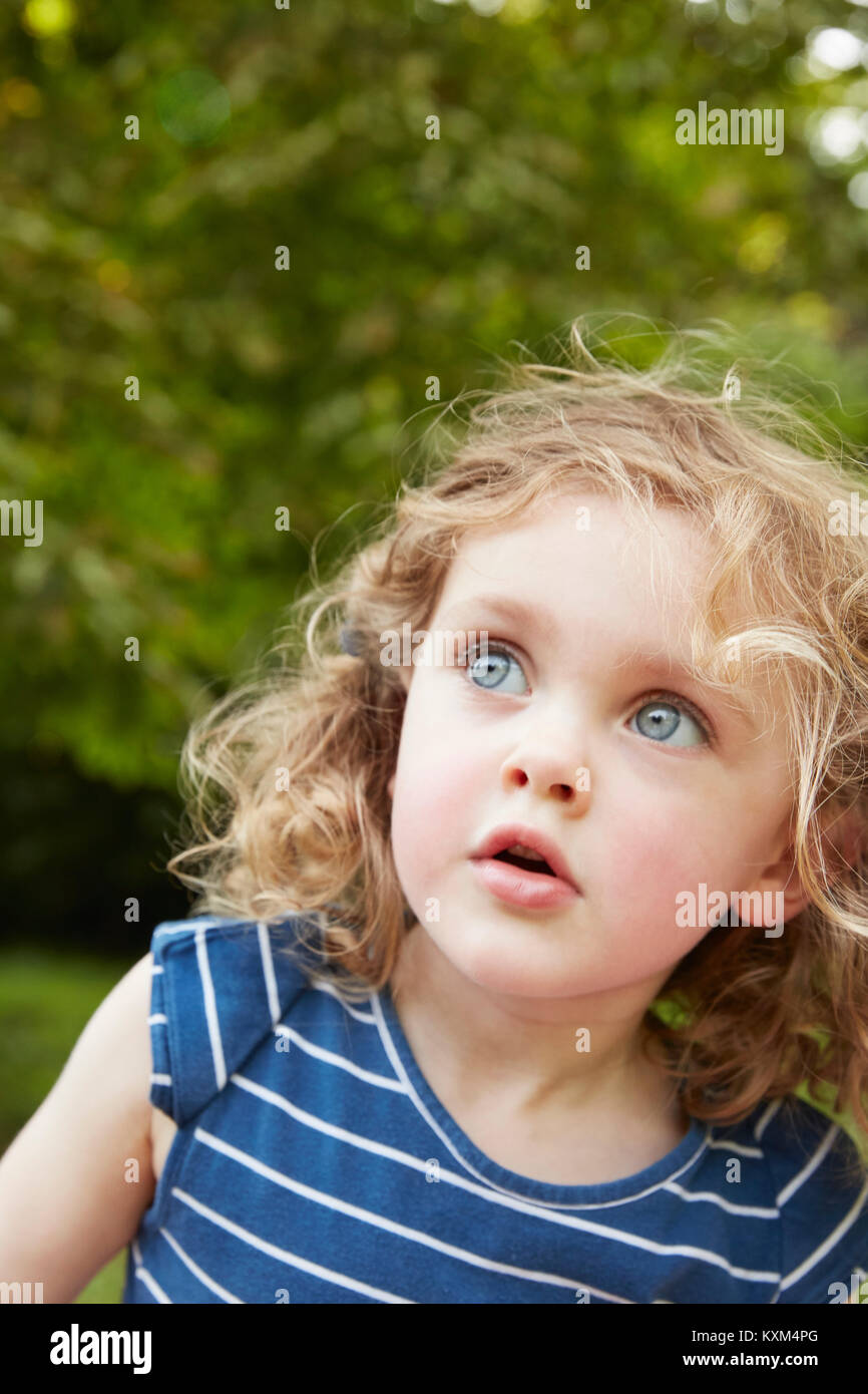 Portrait of blond wavy haired girl with blue eyes gazing in park Stock Photo
