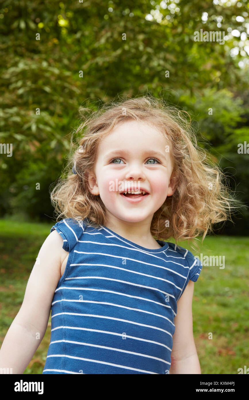 Portrait of blond wavy haired girl with blue eyes in park Stock Photo