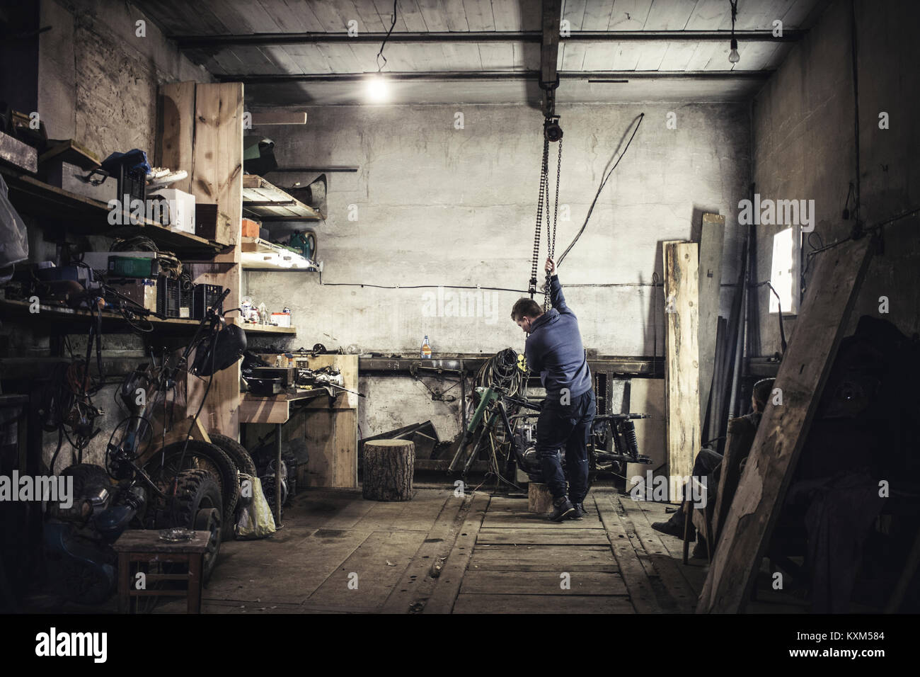 Mechanic hoisting dismantled vintage motorcycle in workshop Stock Photo