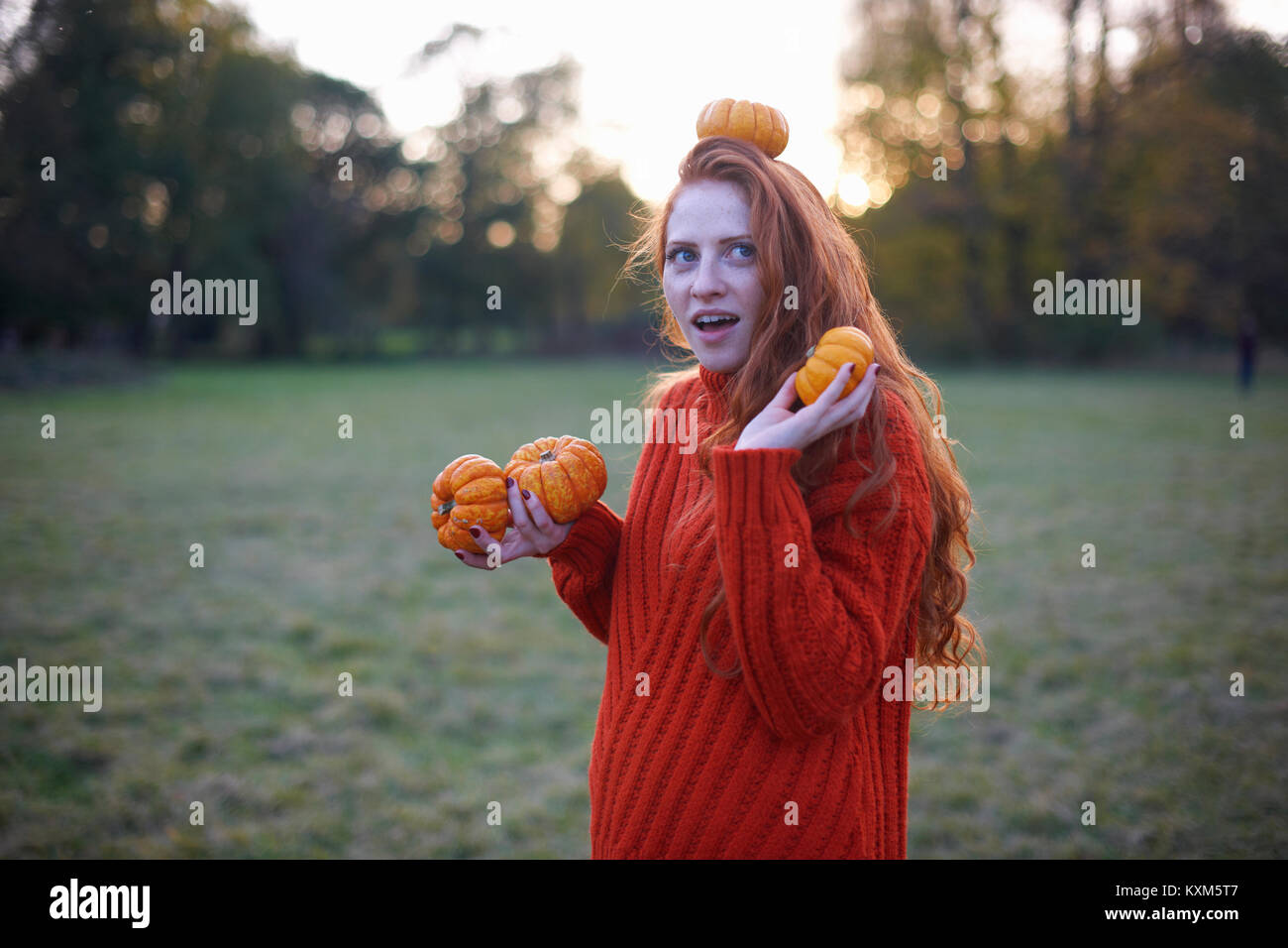 Young woman in rural setting,holding pumpkins,pumpkin balanced in head Stock Photo