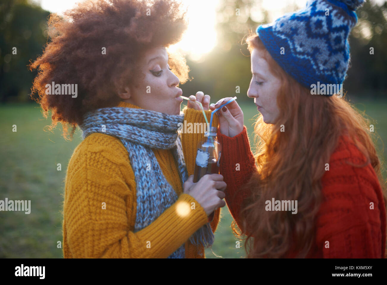 Two young women,in rural setting,drinking from bottle with straws Stock Photo