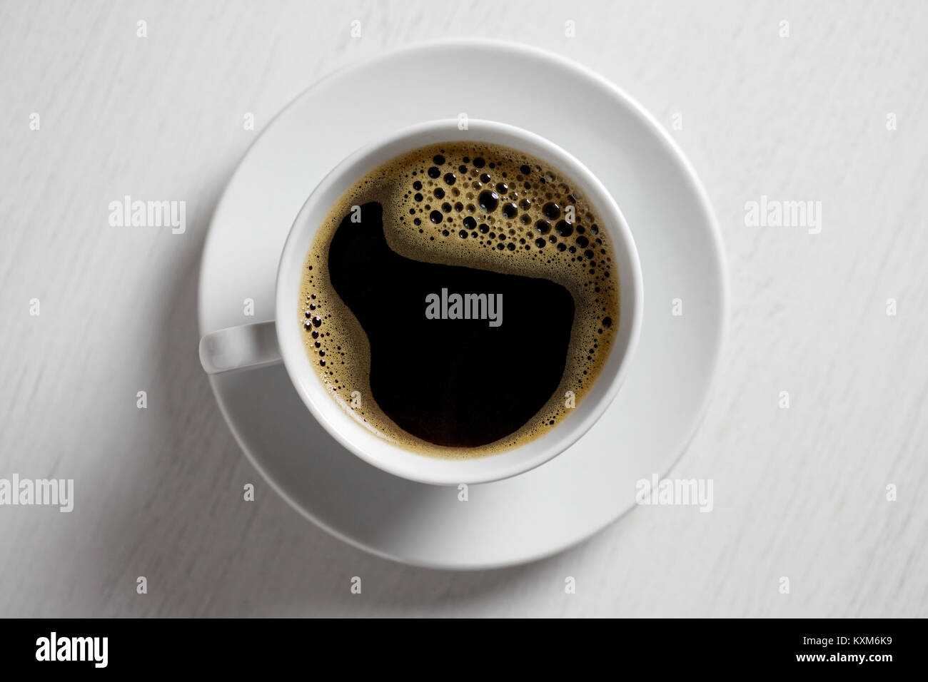 Freshly poured black coffee with froth in white ceramic cup isolated on white from above. Stock Photo