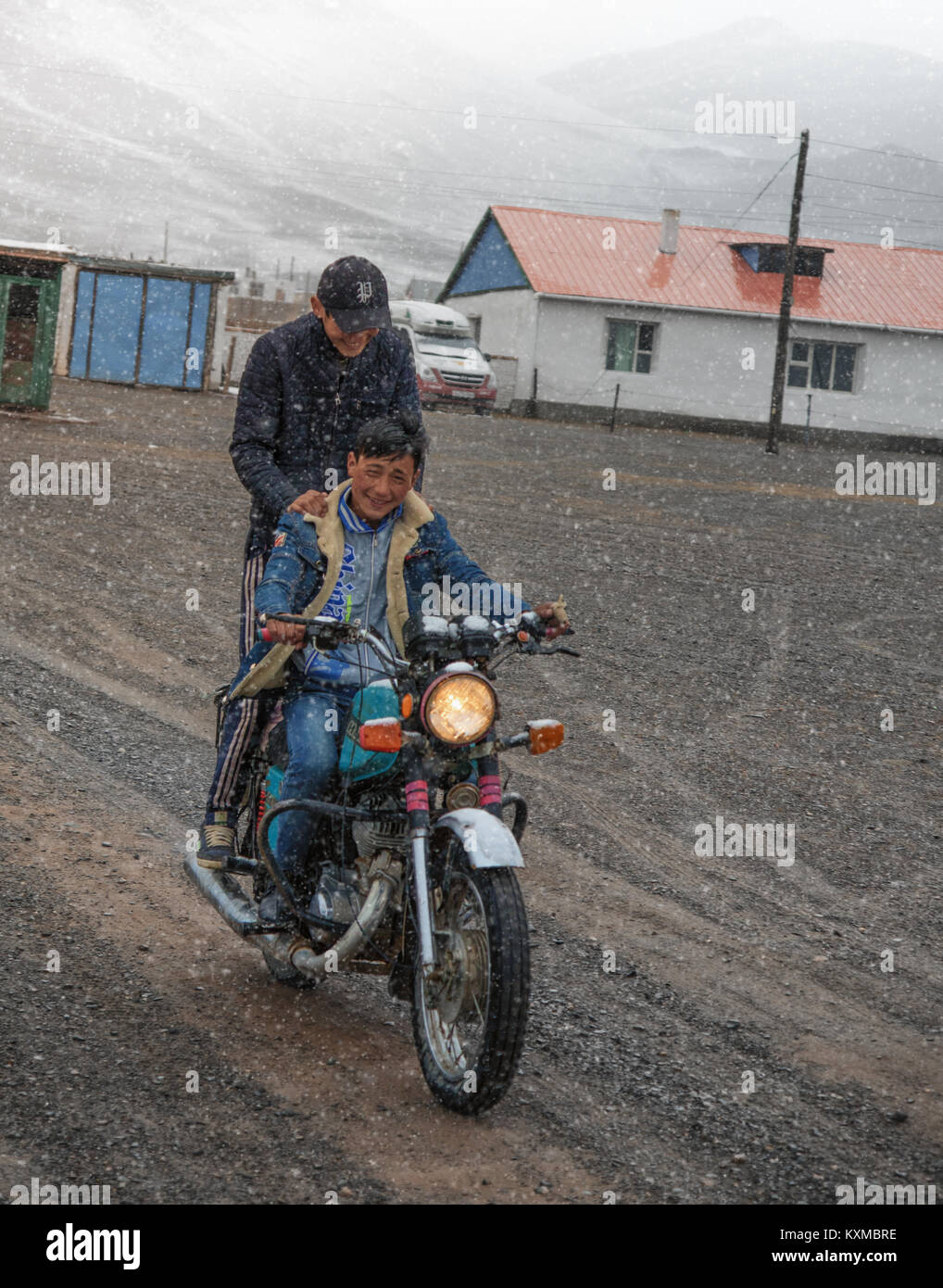 Country side rural two young men riding motorbike snow winter cold Mongolia town Stock Photo