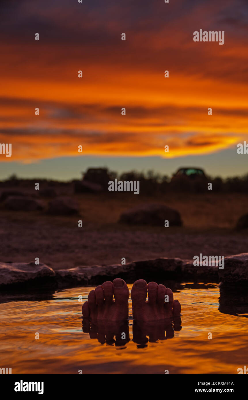 toes and feet poking out of a hot spring at sunset with reflection in the water and selective focus Stock Photo