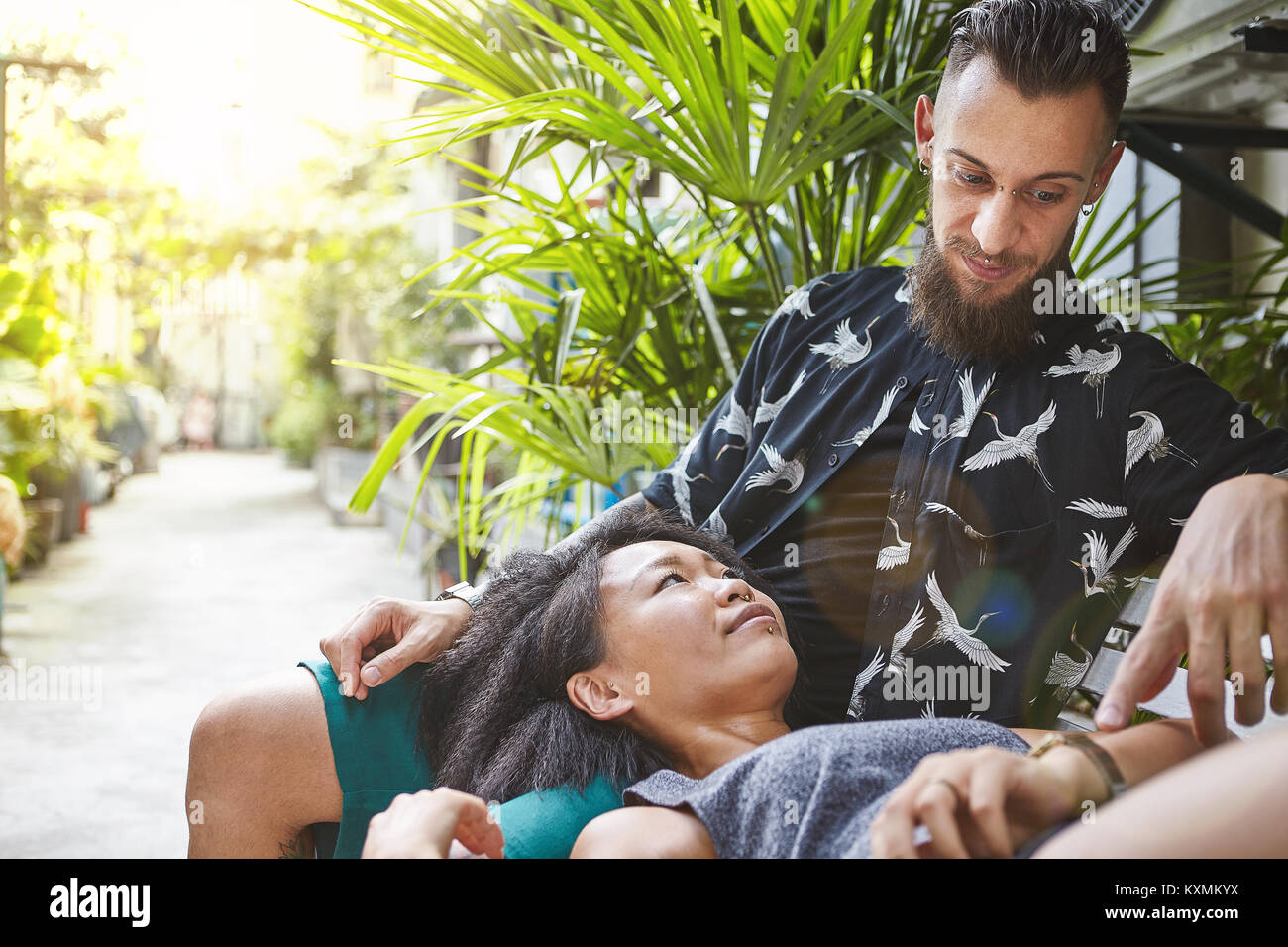 Multi ethnic couple reclining on garden bench in residential alleyway