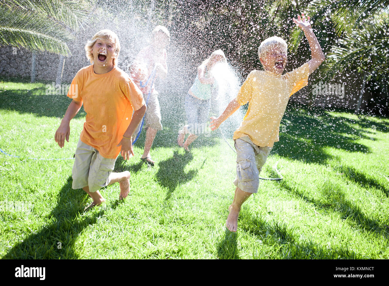 Parents in garden spraying sons with water from hosepipe Stock Photo