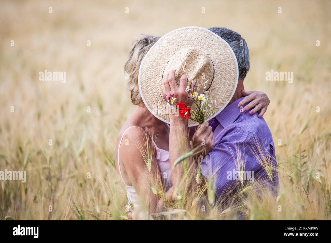 Couple in field in tall grass covering faces with straw hat Stock Photo