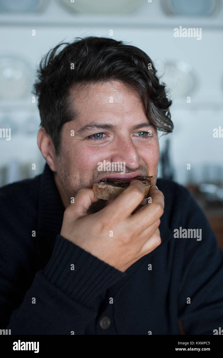 Mid adult man snacking on bread and jam in kitchen Stock Photo