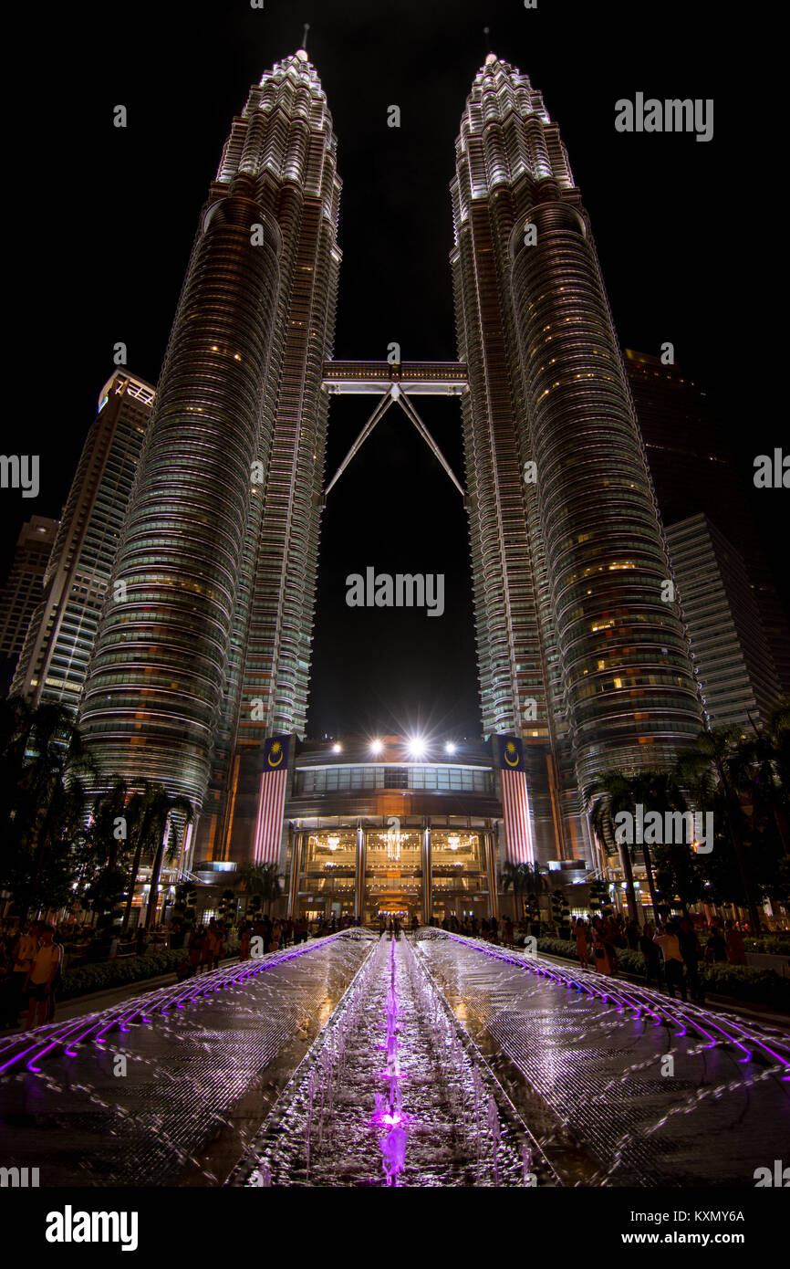 Low angle of the Petronas twin towers, Kuala Lumpur, Malaysia with purple illuminated fountain in the foreground. Stock Photo