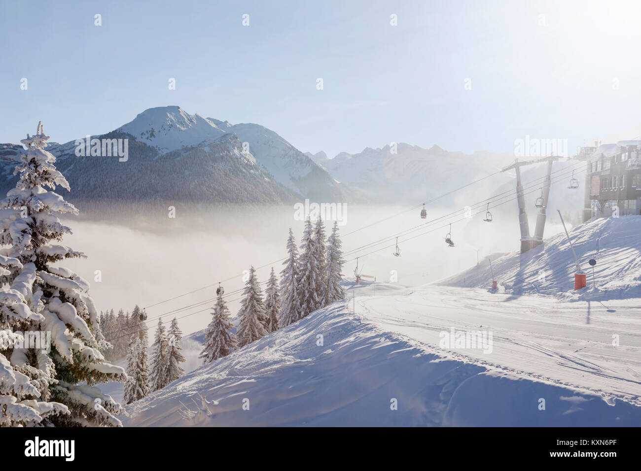 Morning view of Morzine ski resort with snow covered trees, groomed piste, ski lifts and misty mountains in the Portes du Soleil ski area, France. Stock Photo
