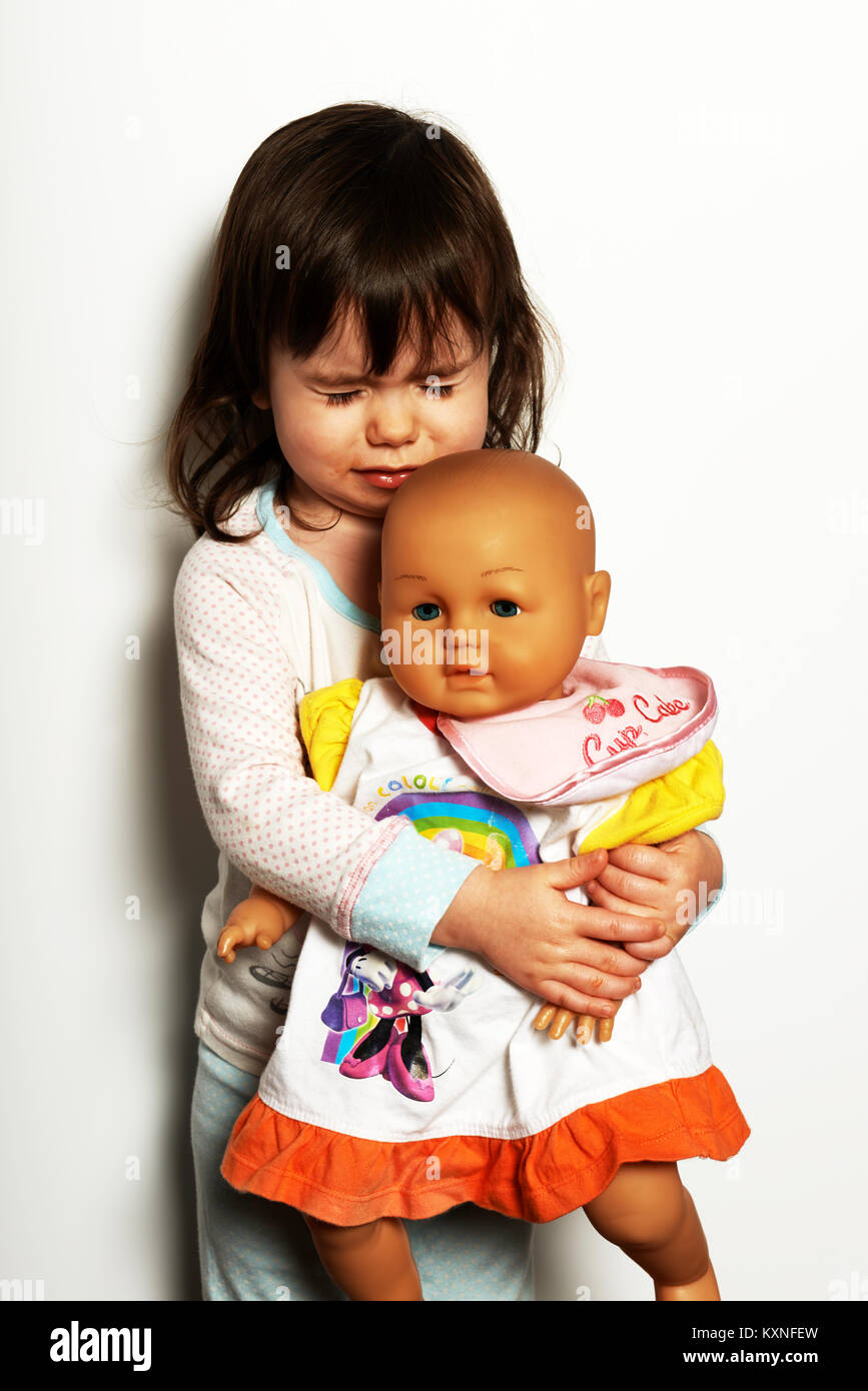3 year old girl crying while holding baby doll Stock Photo