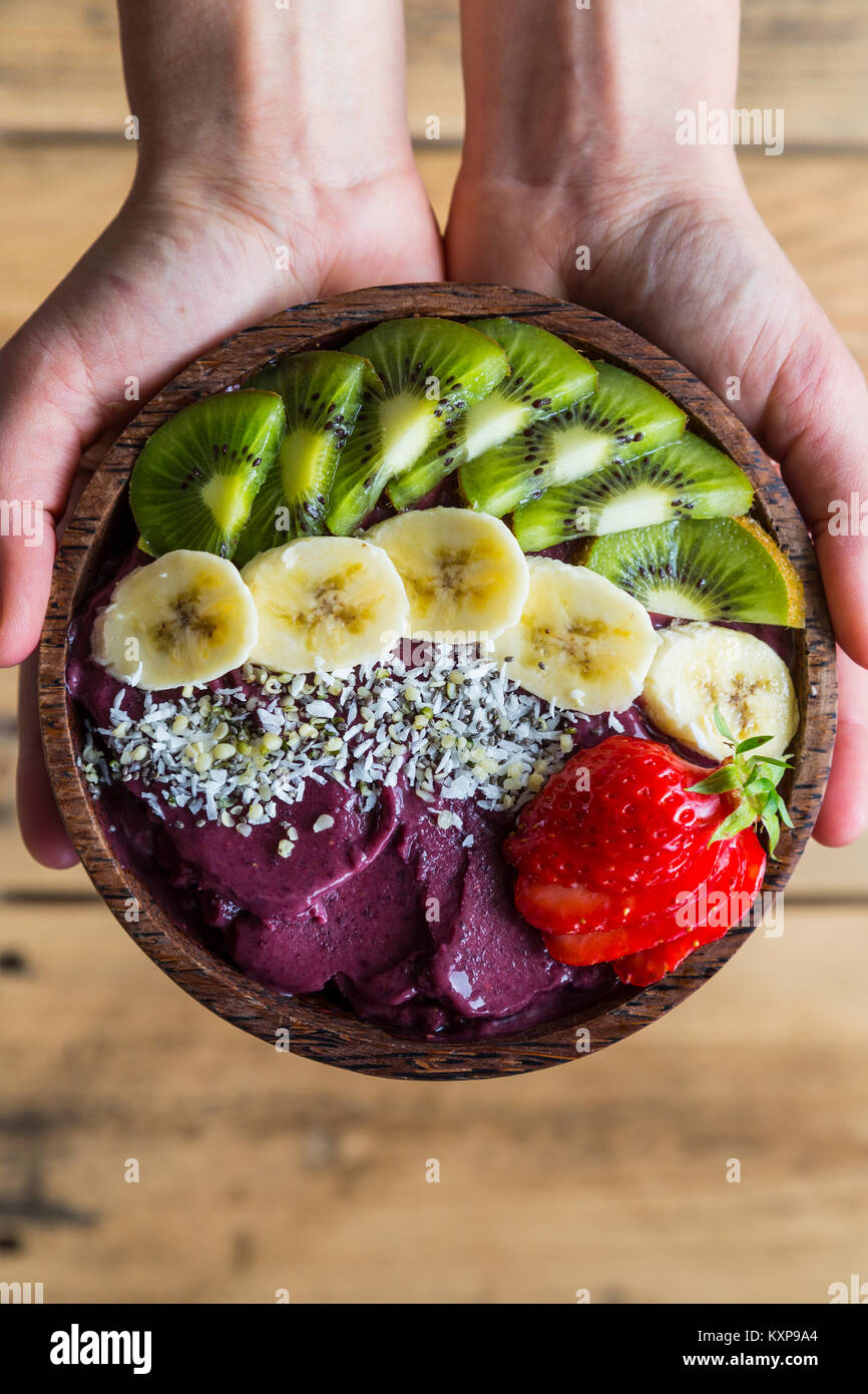 Acai bowl in hands Bowl of acai purée with toppings of banana, kiwi, strawberry and seeds