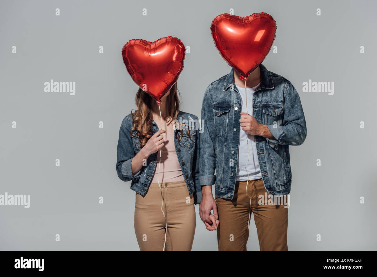 young couple hiding faces behind red heart shaped balloons isolated on ...