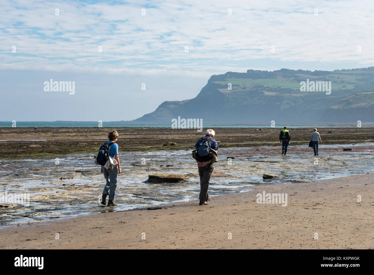 Walkers on the beach at Robin Hood's Bay, North Yorkshire, England. A sunny September morning looking towards Ravenscar. Stock Photo